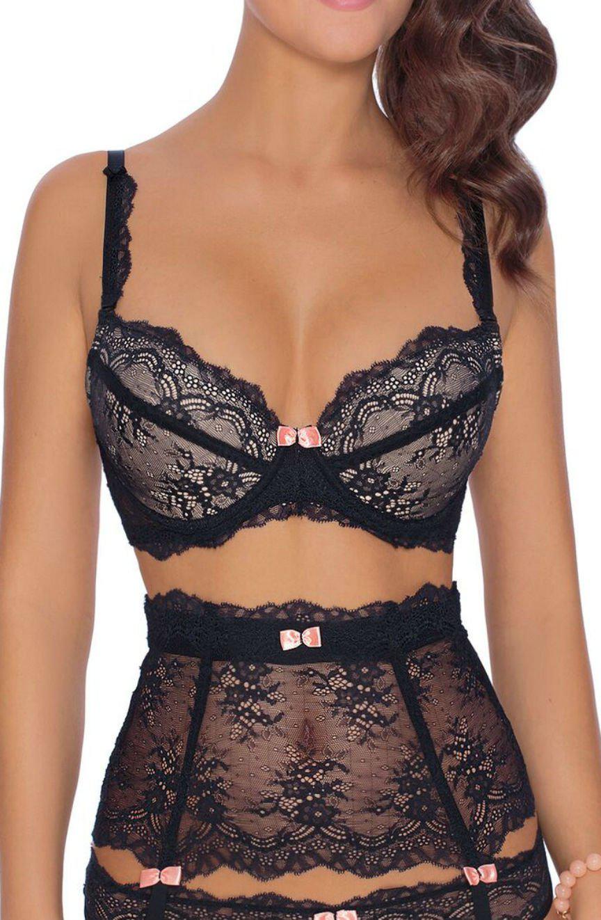 A person is wearing the Roza Ambre Push Up Bra Black, a romantic black lace lingerie set from Roza, featuring pink bow accents and a matching high-waisted garter belt. The intricately patterned lingerie complements the person's hair styled in loose waves. The photo is cropped to show only the torso and upper thighs.