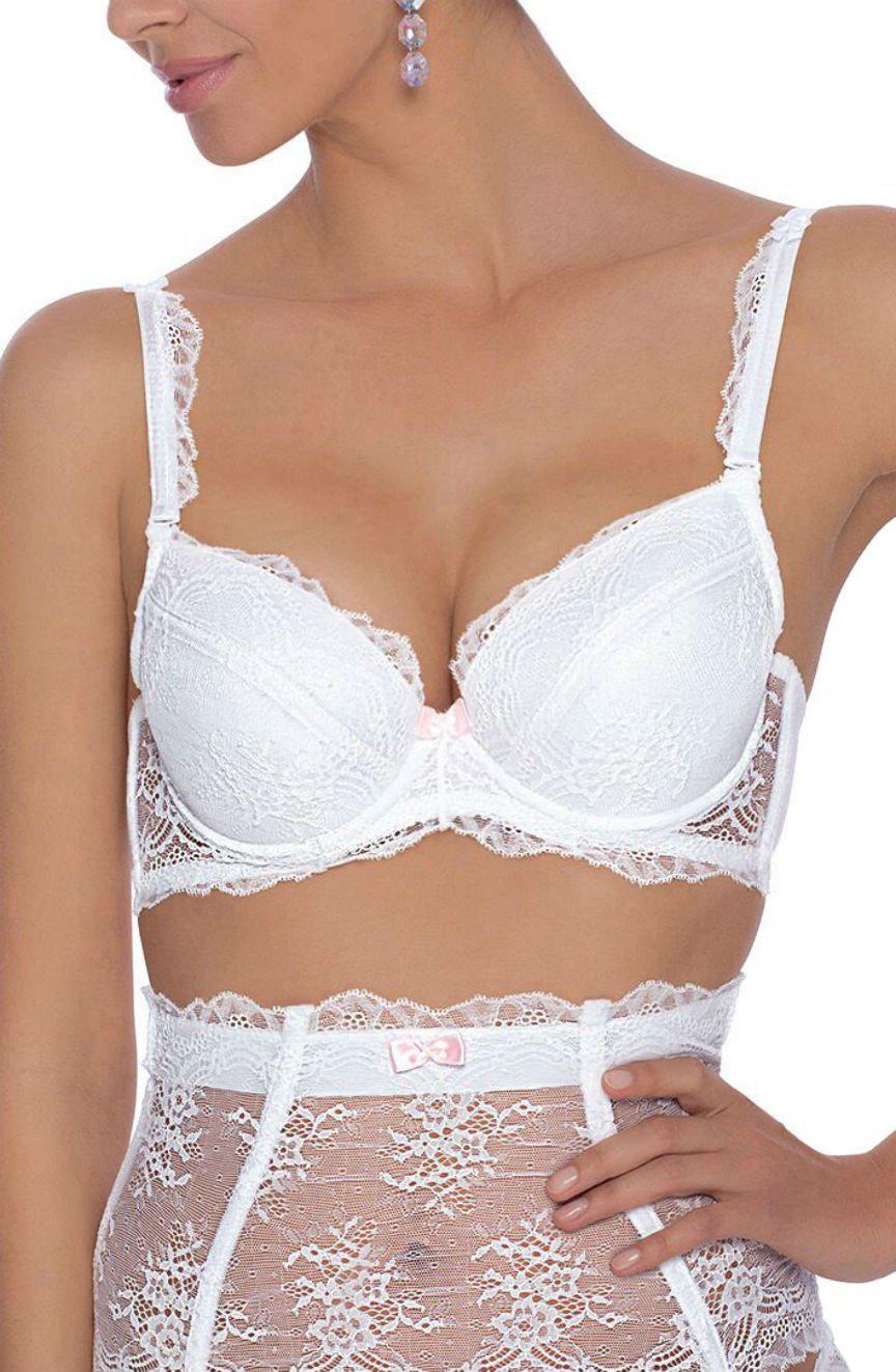 A person wearing the Roza Ambre Push Up Bra White, paired with high-waisted stockings adorned with small pink bows, showcases a romantic and feminine look. Only the upper body is visible, complemented by purple dangling earrings from the Ambre collection.