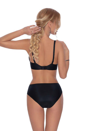 A woman stands with her back to the camera, elegantly showcasing the Roza Ambre Soft Cup Bra Black from the Ambre collection, paired with high-waisted panties. Her long, wavy blonde hair is pulled into a loose ponytail. She adjusts her bra strap with one hand and has her other arm bent by her side.