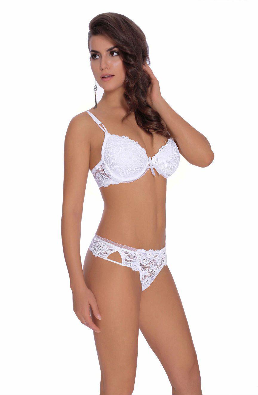 A woman wearing a Roza Carmen White Bra and a matching lacy thong from the Roza collection stands against a plain white background. She has long, wavy hair and wears an earring. She is looking off to the side with one hand touching her hair.