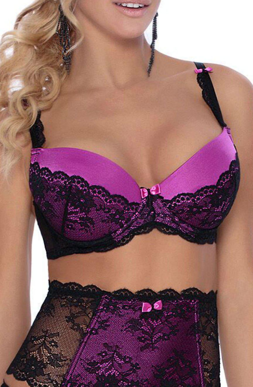 A woman with blonde hair is adorned in the sophisticated Roza Fifi Push Up Bra Black, a purple and black lace lingerie set accented with pink bows. The matching high-waisted panty showcases exquisite lace details. She complements her look with long, dark earrings, while her face remains out of sight in the image.