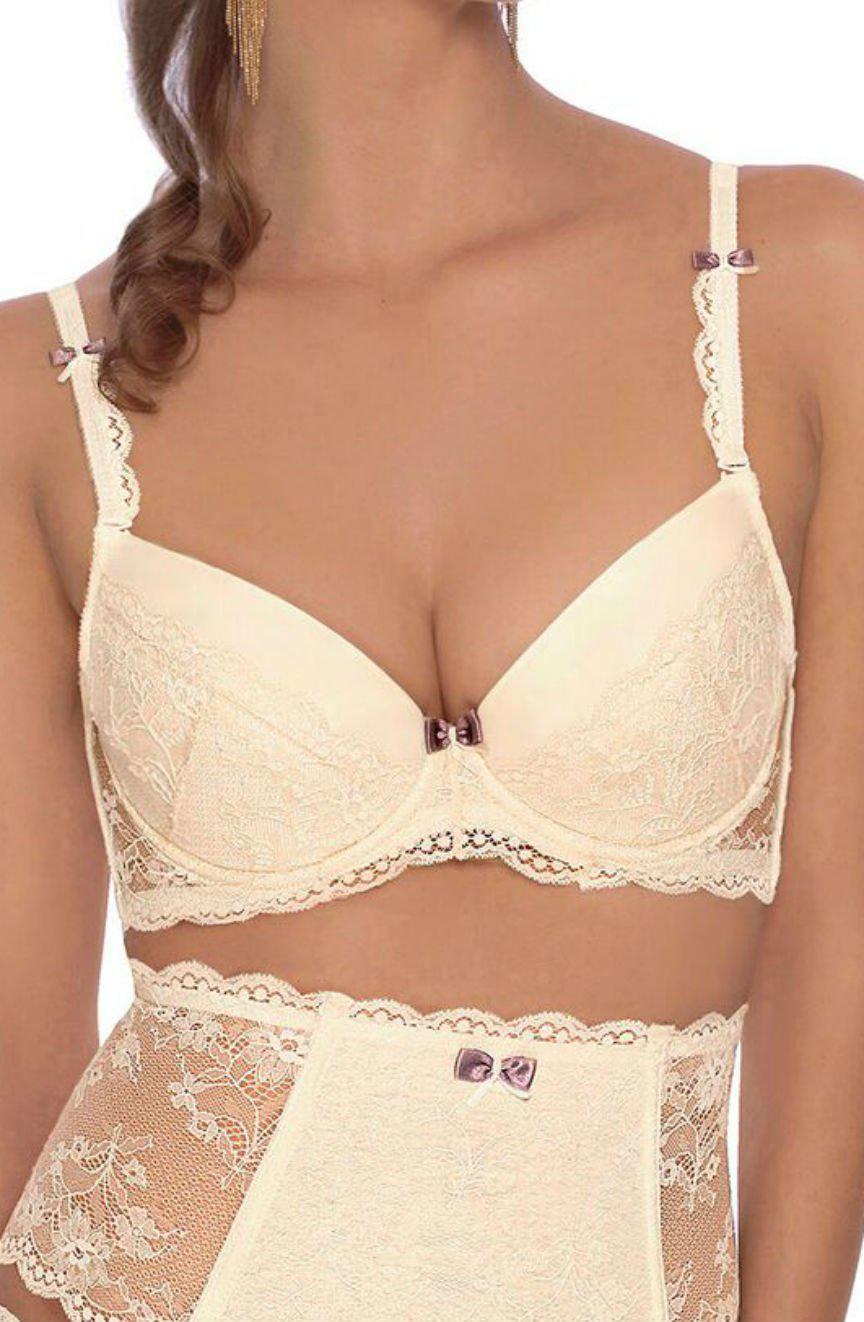 A woman is wearing a matching set of ivory-colored lingerie, featuring the elegant Roza Fifi Push Up Bra and high-waisted lace panties. Both the bra and panties are embellished with small purple bows. Her hair cascades in loose curls, complemented by her long, dangling earrings.