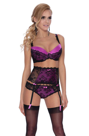 A woman with long, wavy blonde hair is wearing the Roza Fifi Suspender Belt Black from the brand Roza. The delicate lace design includes a push-up bra, high-waisted garter belt, and panties, all accented with small purple bows. She is also wearing black thigh-high stockings. She poses confidently with a slight smile.