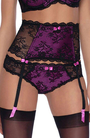 A person wearing the Roza Fifi Thong Black lingerie set, featuring a purple and black lace push-up bra, garter belt, and panties adorned with small pink bows. The suspender belt has black straps connected to black stockings.