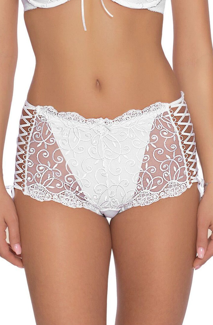 A woman is wearing the Roza Ginewra Short White lingerie set by Roza, featuring intricately designed white lace with sheer panels and floral embroidery, perfect for bridal wear. The set includes a matching push-up bra with lace-up details on the sides and lace trim at the edges. Her midsection is visible, but her face is not shown in the image.