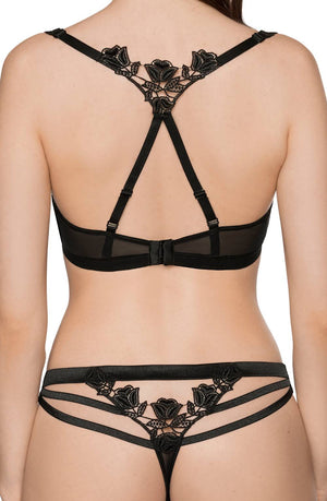 A woman is seen from the back wearing a black lingerie set from Roza. The Roza Lisbet Black Soft Cup Bra boasts intricate floral lace detailing and straps forming a unique pattern on the back. Matching panties feature similar floral lace, multiple thin straps, and are complete with embroidered appliques.