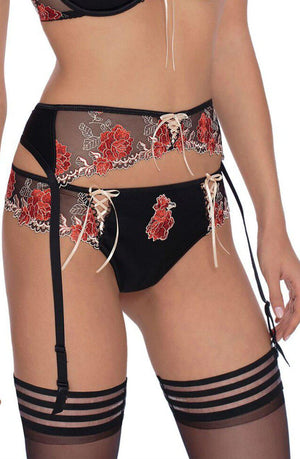 A woman wearing the Roza Natali Black Suspender Belt and matching lingerie set, featuring pink and white floral embroidery, paired with a matching garter belt and stockings. The top includes sheer panels and intricate lace-up details. The image focuses on her torso and hips.