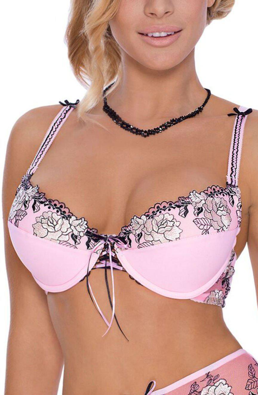 A woman with blonde hair is seen wearing a Roza Natali Pink Bra by Roza, featuring black and white floral embroidery, a black ribbon detail in the center, and thin straps adorned with small bows. She's also accessorizing with a black beaded necklace. Only her upper body is visible.