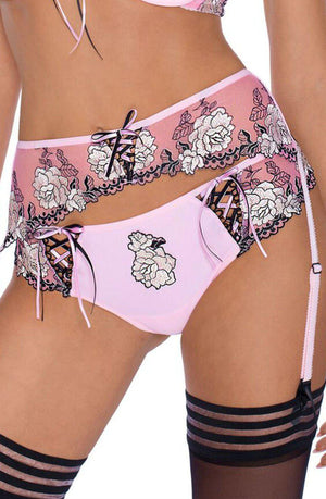 A close-up image of a person wearing the Roza Natali Pink Brief set by Roza, which features black lace trim and white floral embroidery. The set includes a bra, garter belt, and panties. The person is also adorned with black stockings that have a few horizontal stripes at the top.