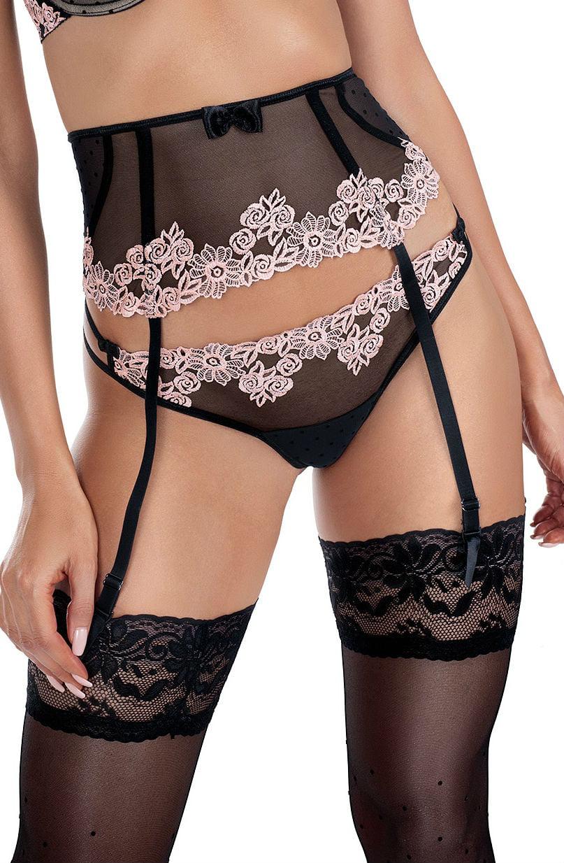 A woman is wearing the black and salmon Roza Nefer Thong by Roza, which features sheer fabric with intricate floral lace patterns. She complements her lingerie with a garter belt and stockings, a push-up bra, and black straps. She is posing with one hand resting lightly on her hip.