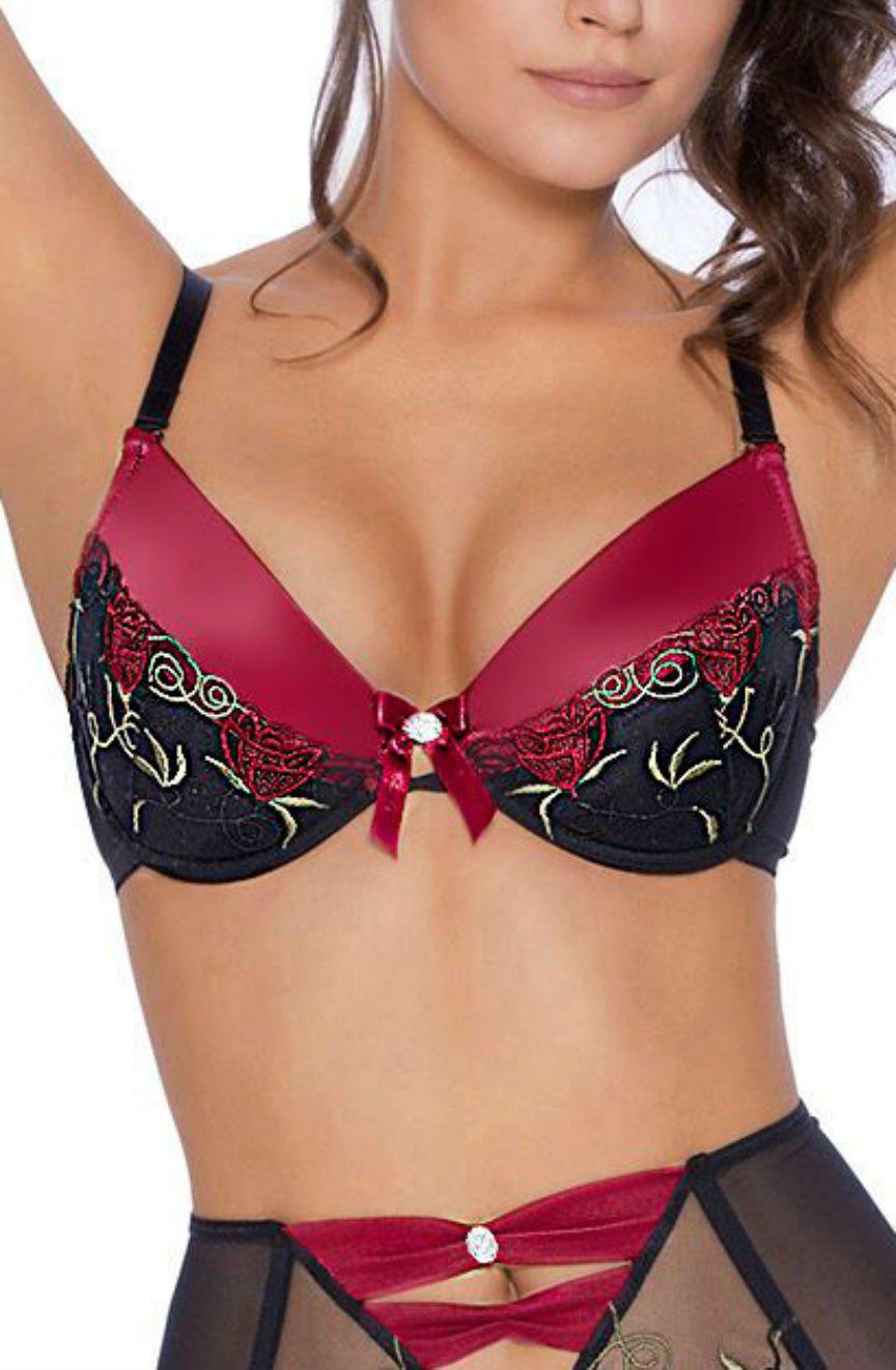 A woman models the Roza Rufina Push Up Bra Black by Roza, showcasing its deep red and black color scheme with intricate lace detailing, soft push-up cups, and small decorative bows. The bra is designed with a black lace overlay and floral embroidery, while the matching bottoms are partially visible featuring a similar design.