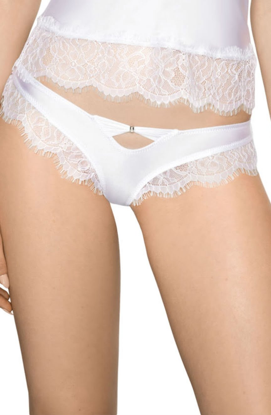 A woman wears a white lace-trimmed lingerie set. The satin fabric boasts delicate eyelash lace accents around the edges. The briefs, the Roza Sija White Brief by Roza, feature a cut-out design at the front that reveals a small triangular section, leaving only her midsection and thighs visible.