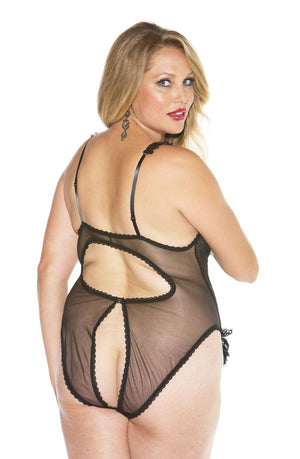 A woman with long blonde hair is posing confidently in the Shirley Of Hollywood Xx2497 Black Teddy, a sheer lingerie bodysuit featuring decorative cut-outs on the back and crafted from stretch lace by Shirley of Hollywood. She enhances her look with dark lipstick and chandelier earrings against a plain white background.